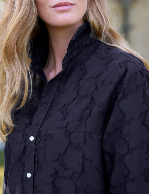 Close-up of a woman wearing a black textured dress with white buttons., alternate view