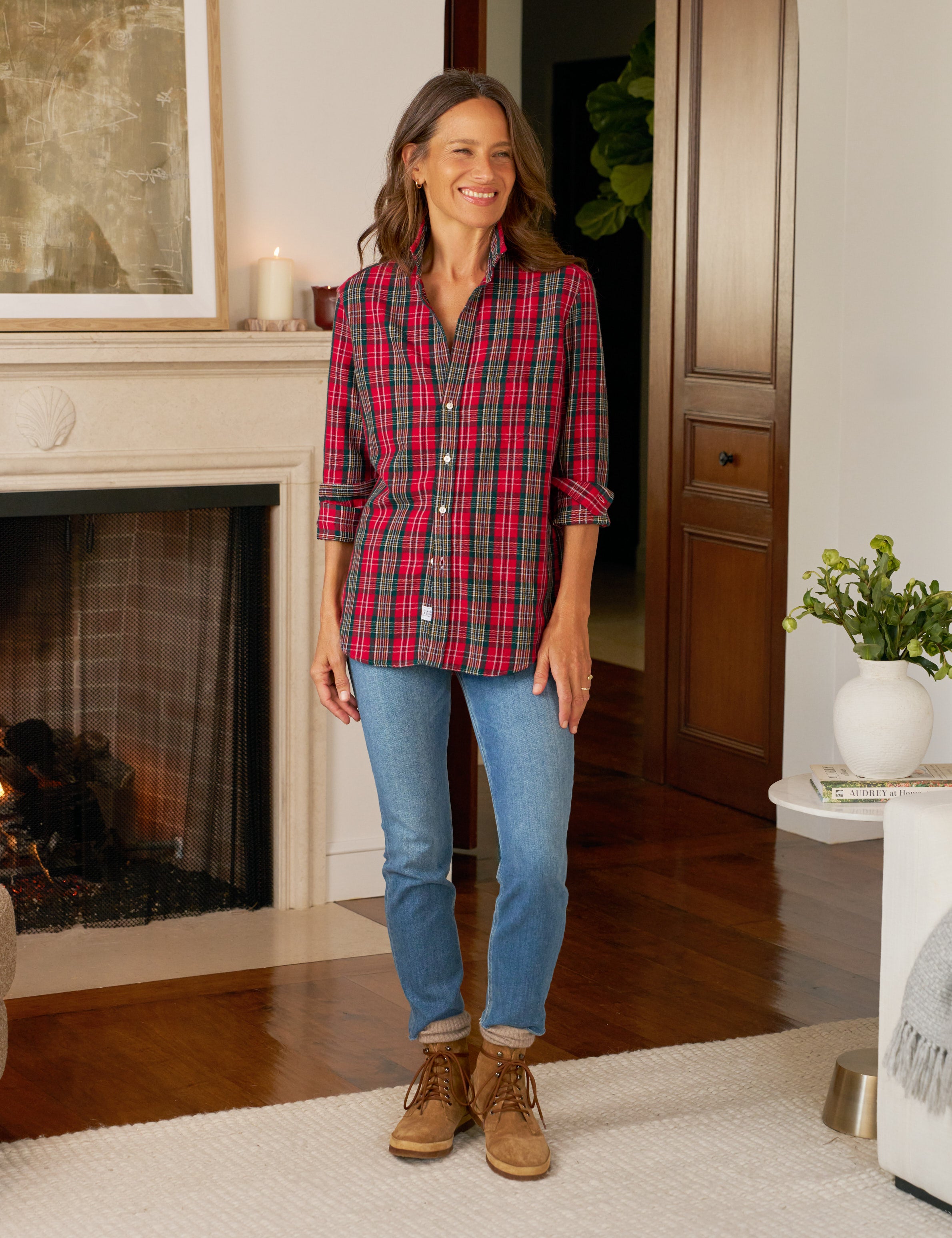 Woman wearing a plaid shirt, jeans, and boots in a cozy living room.
