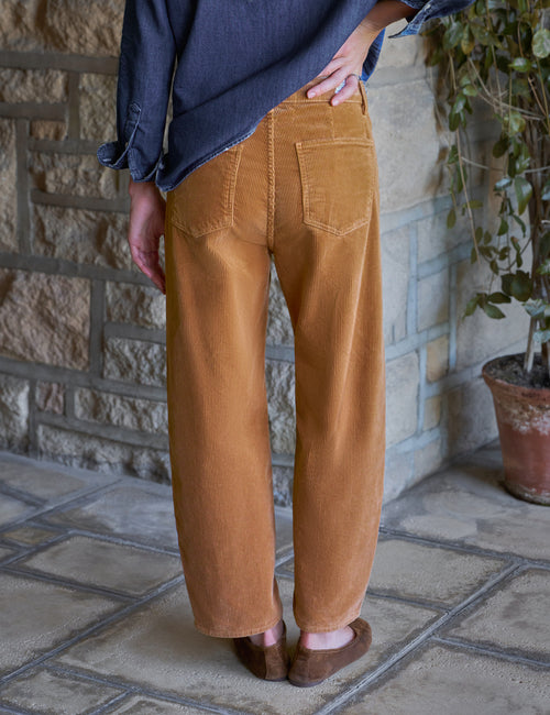 A person shown from the back wearing barrel-leg tan corduroy pants, a dark blue shirt, and brown shoes, standing on a stone patio., view 5