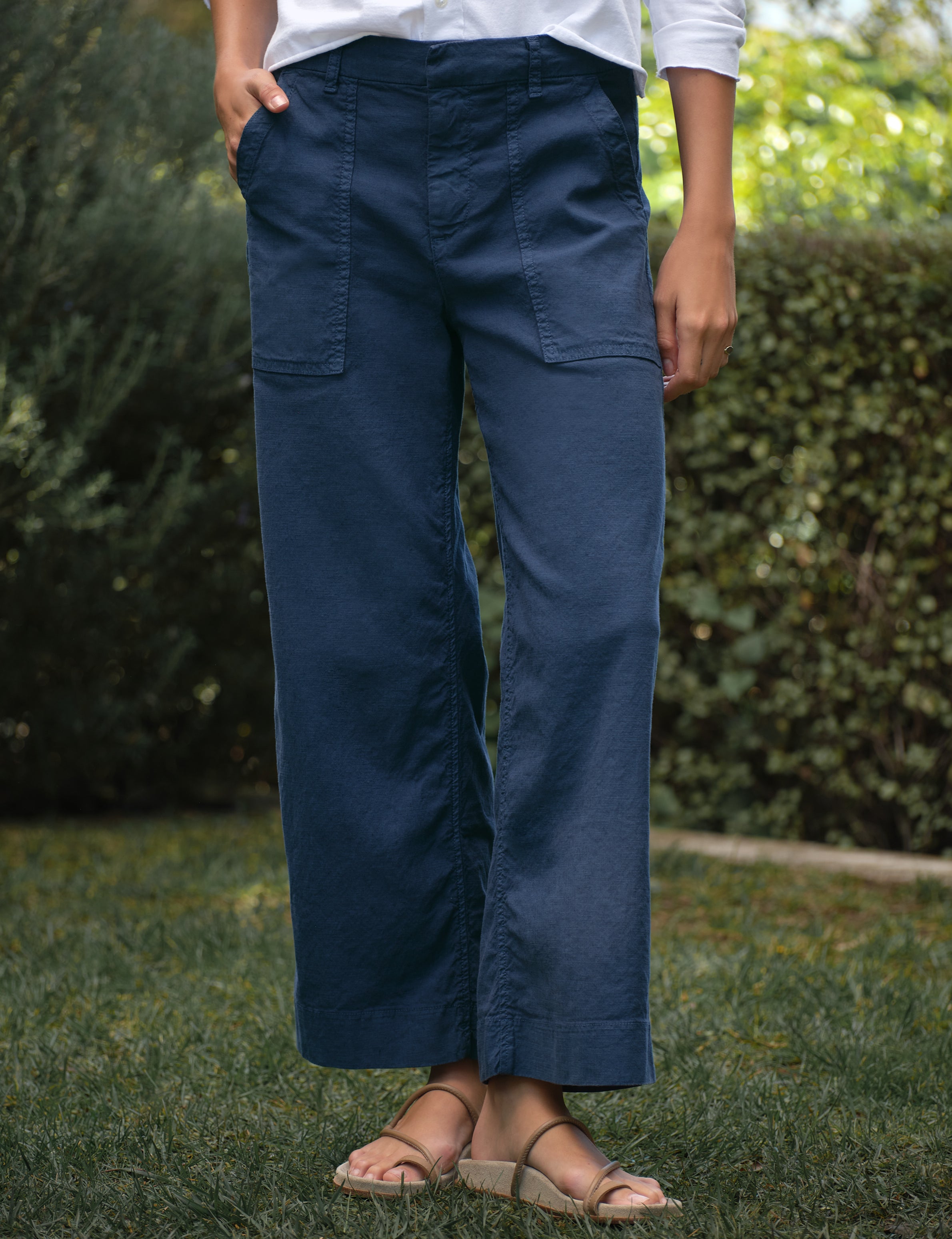 Person wearing navy blue pants standing outdoors with greenery in the background, front view
