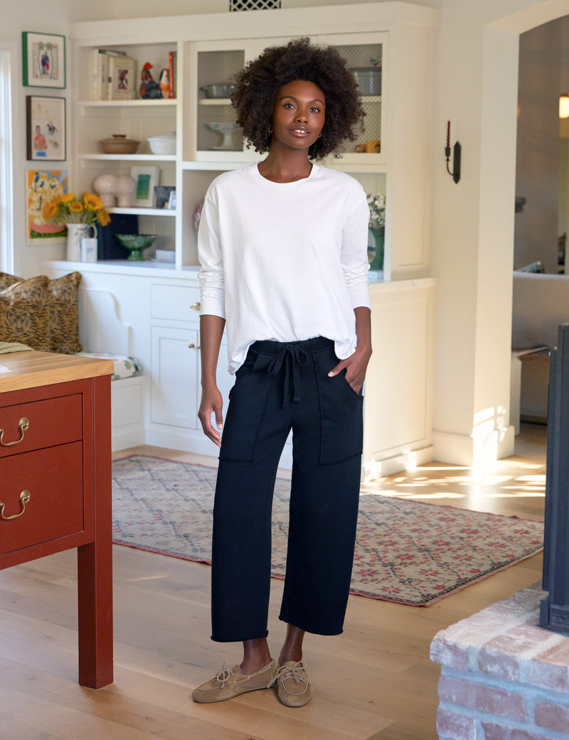Woman standing in a living room wearing a white top and dark pants.