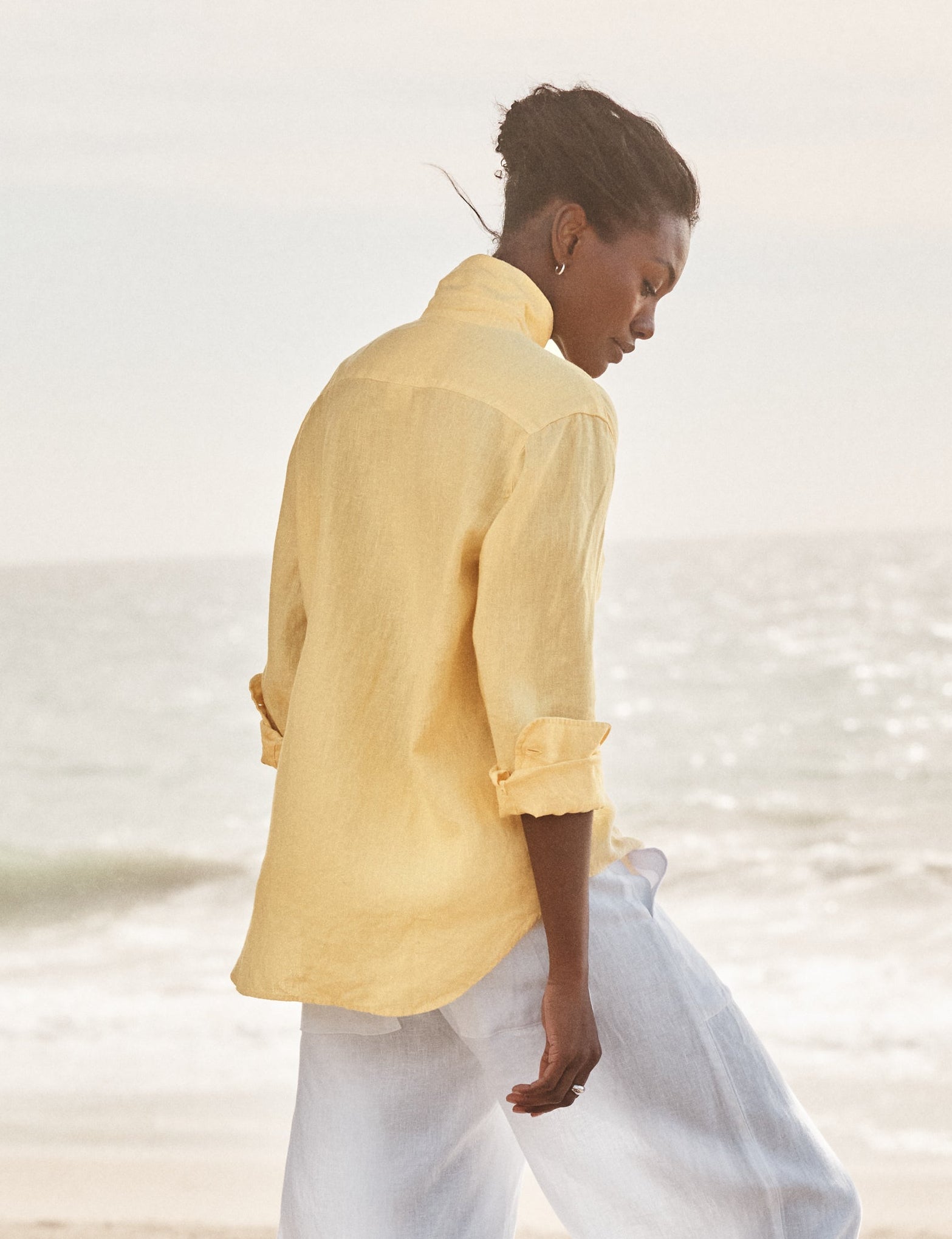 Person wearing a yellow shirt and white pants walking on a beach., alternate view