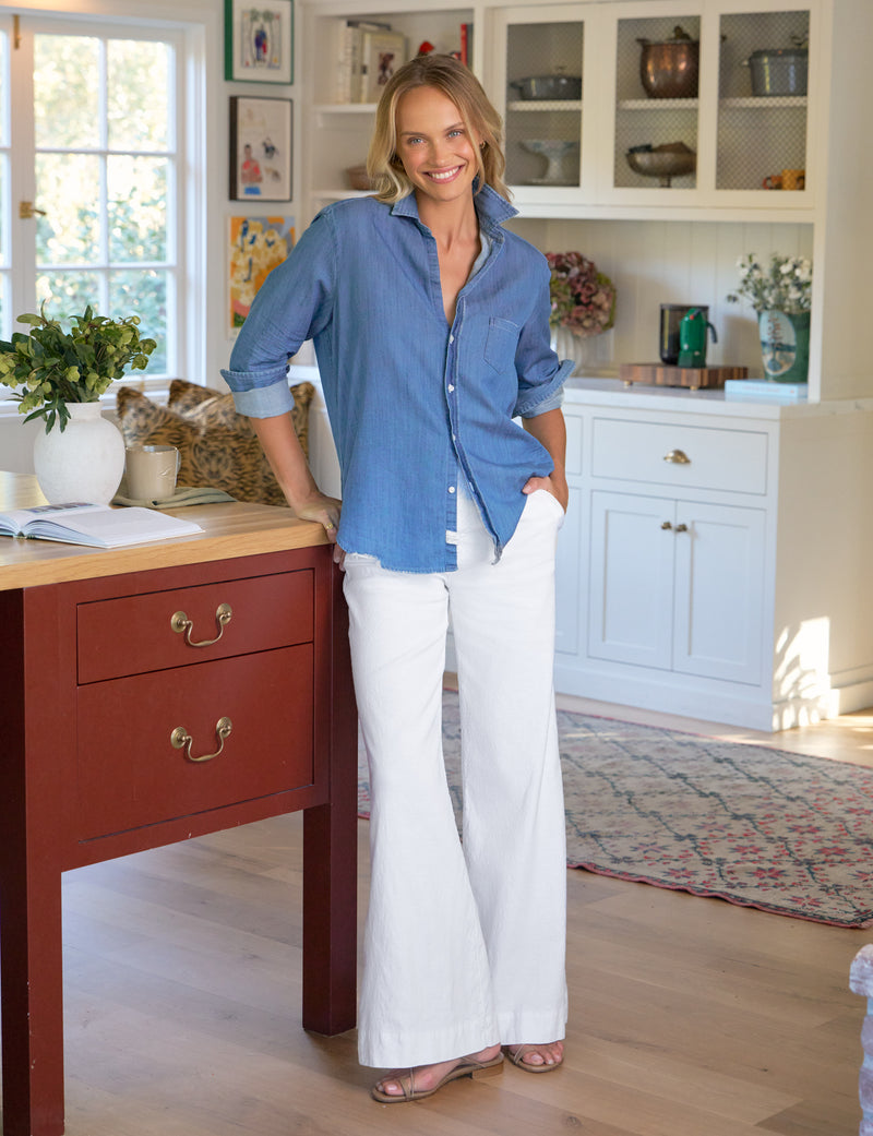 Woman in a blue shirt and white pants standing in a kitchen.