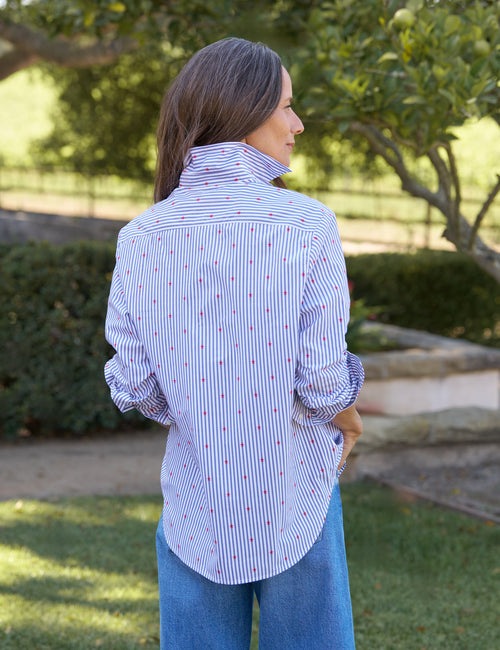 Woman wearing a blue and white striped shirt with red dots outdoors., alternate view