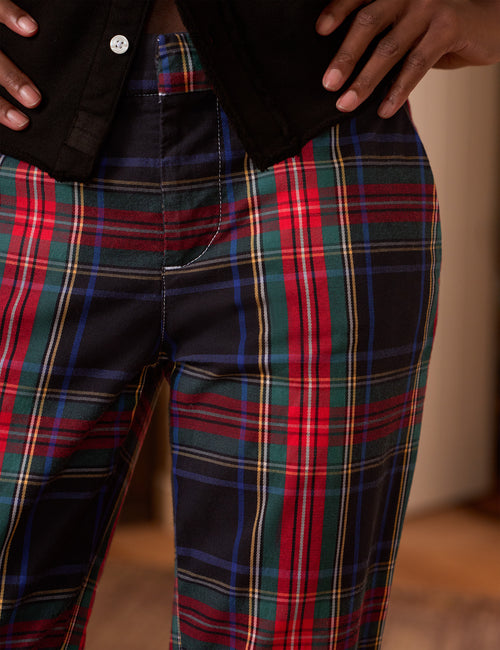 Close-up of a person wearing plaid pants with a black top, showing the lower torso and hands. The pants have a tartan pattern with red, green, blue, yellow, and black stripes., view 3