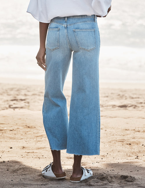 Person wearing blue jeans standing on a sandy surface with a blurred background, alternate view
