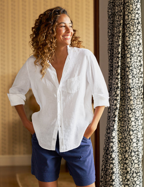 Woman wearing a white shirt and blue shorts standing in a room with patterned curtains., front view