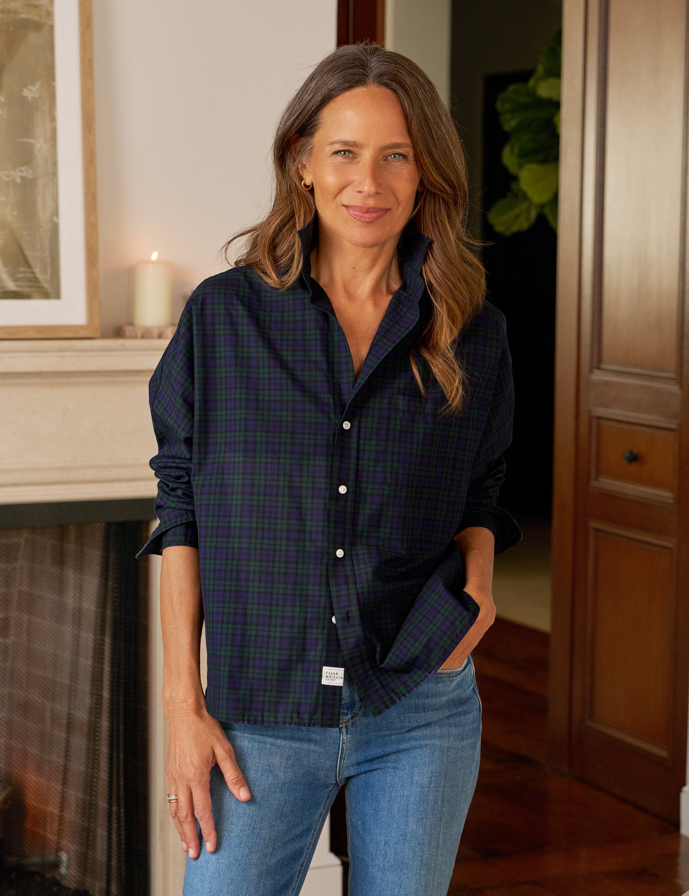 Woman wearing a dark blue plaid shirt and jeans standing in a room with wooden paneling.