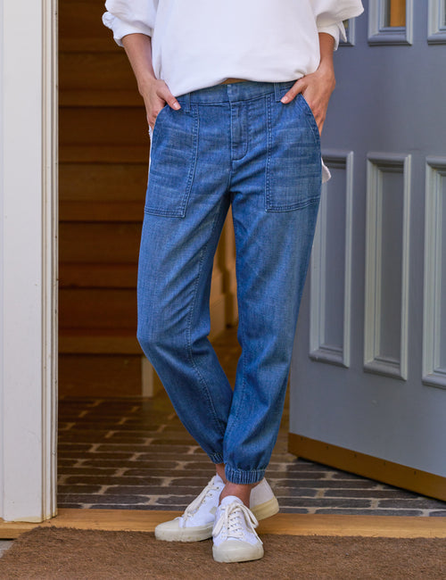 A person standing on a doorstep wearing blue tapered Utility jeans with pockets and white sneakers., front view