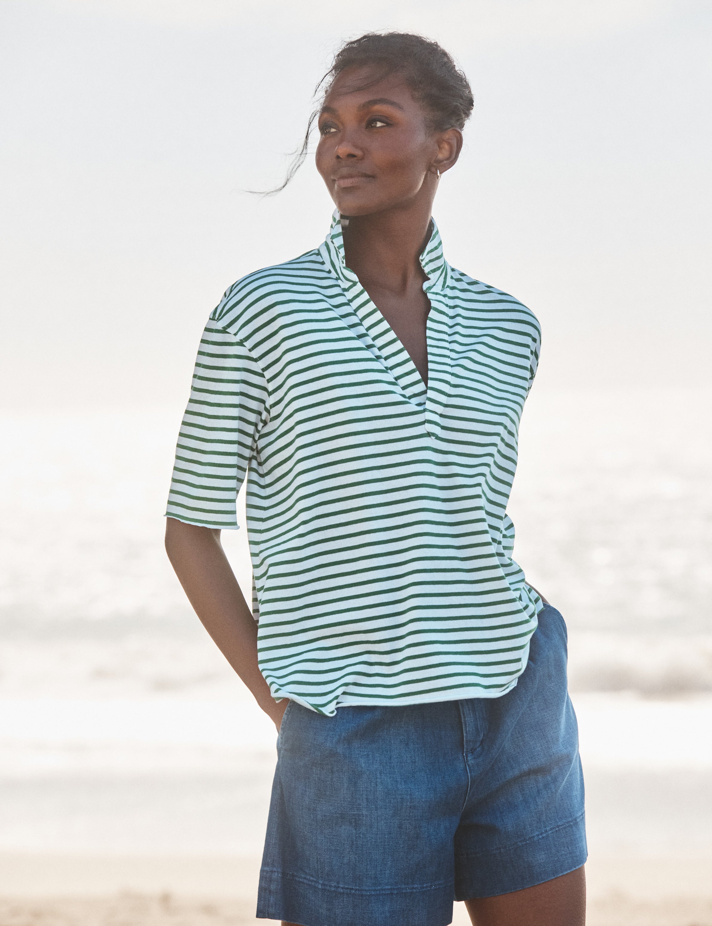 Woman wearing a striped shirt and denim shorts on a beach., front view