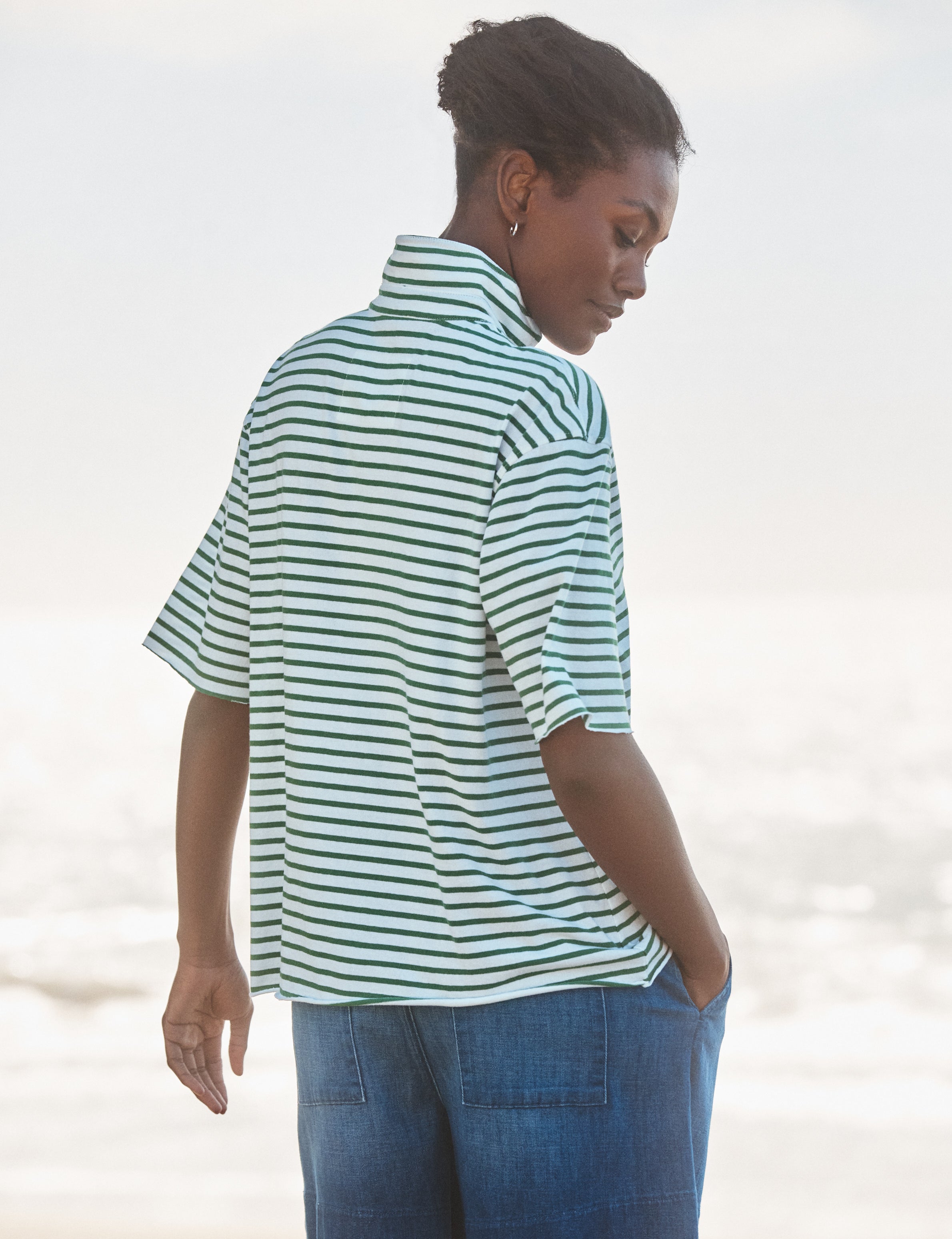 Woman wearing a striped shirt and jeans against a blurred natural background, alternate view