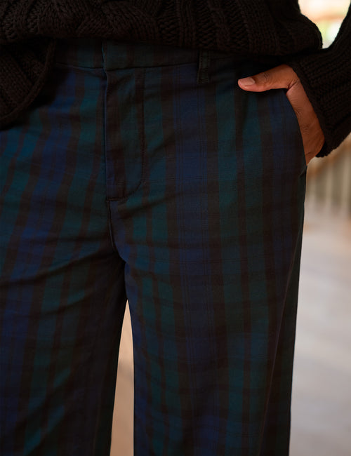 Close-up of a person wearing dark plaid trousers with a black knit sweater, hand in pocket., view 3