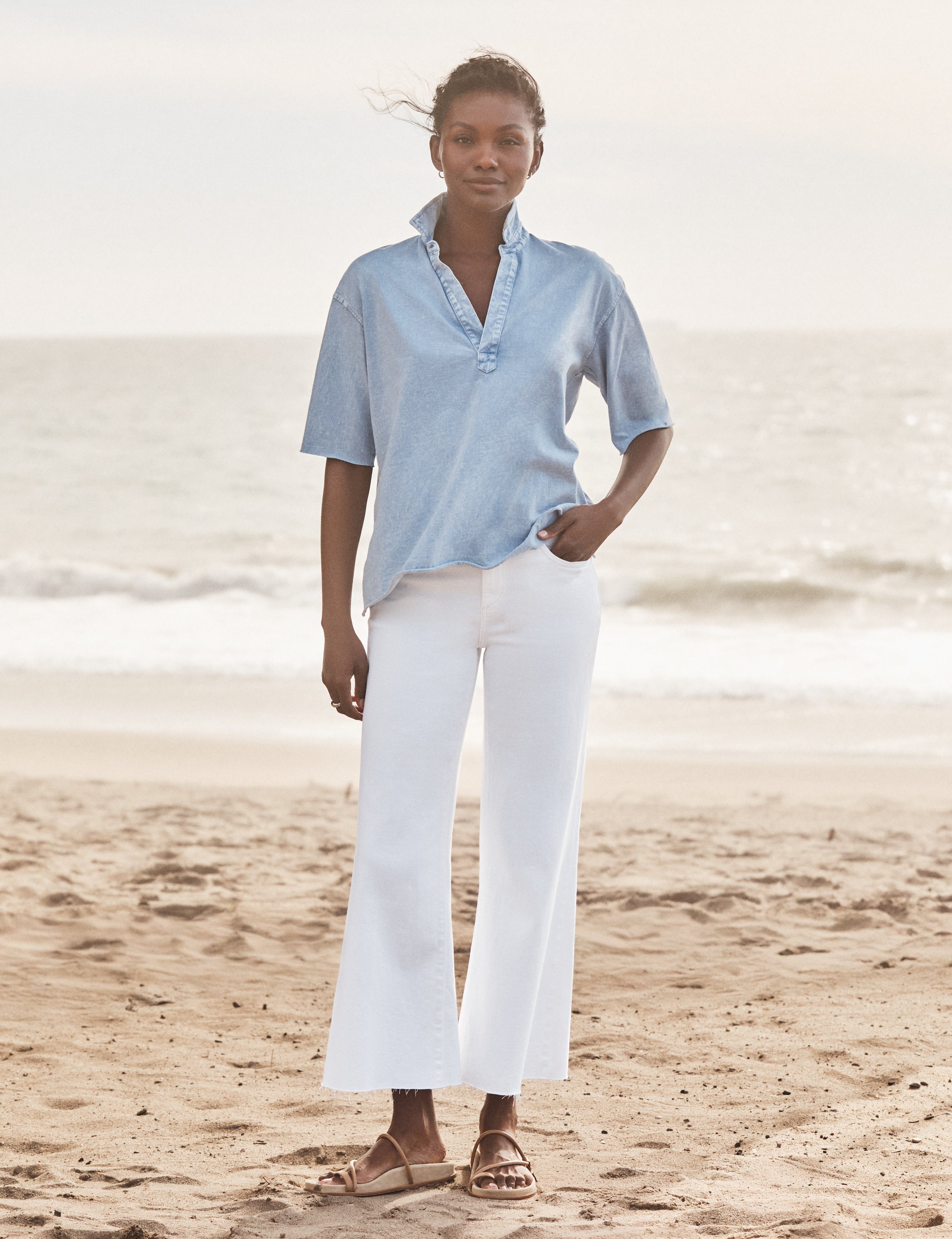 Woman wearing a light blue shirt and white pants standing on a beach., view 5