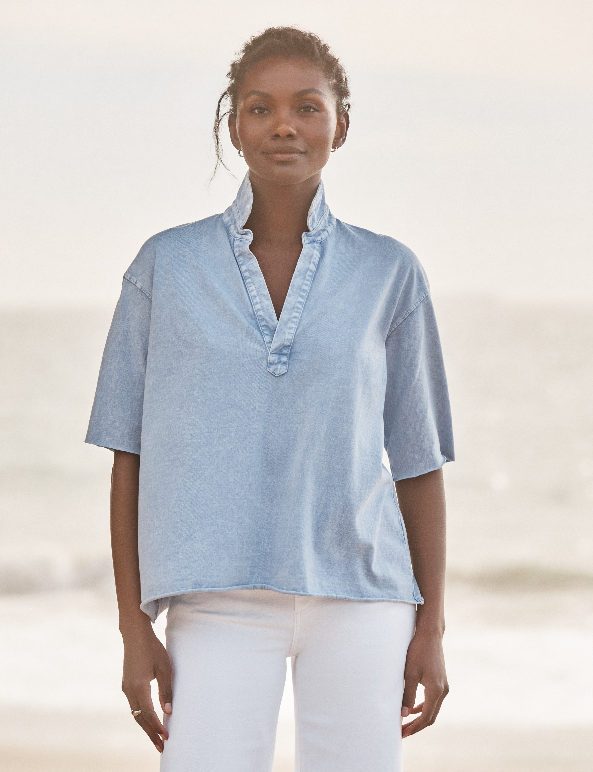 Woman wearing a light blue shirt with a blurred beach background, front view