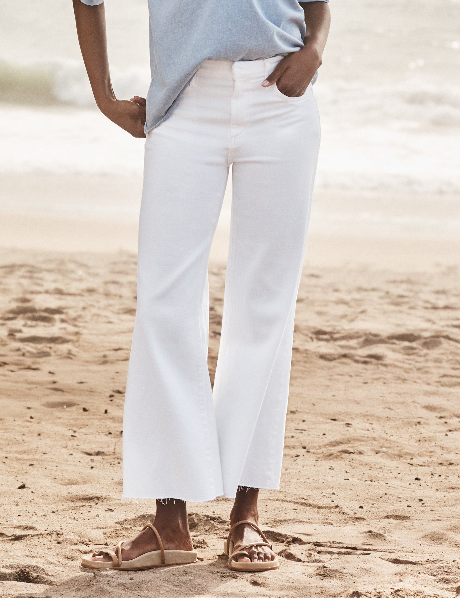 Woman wearing a light blue shirt and white pants on a beach., front view