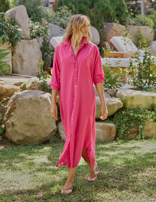 Woman wearing a pink dress standing in a garden with rocks and plants., front view
