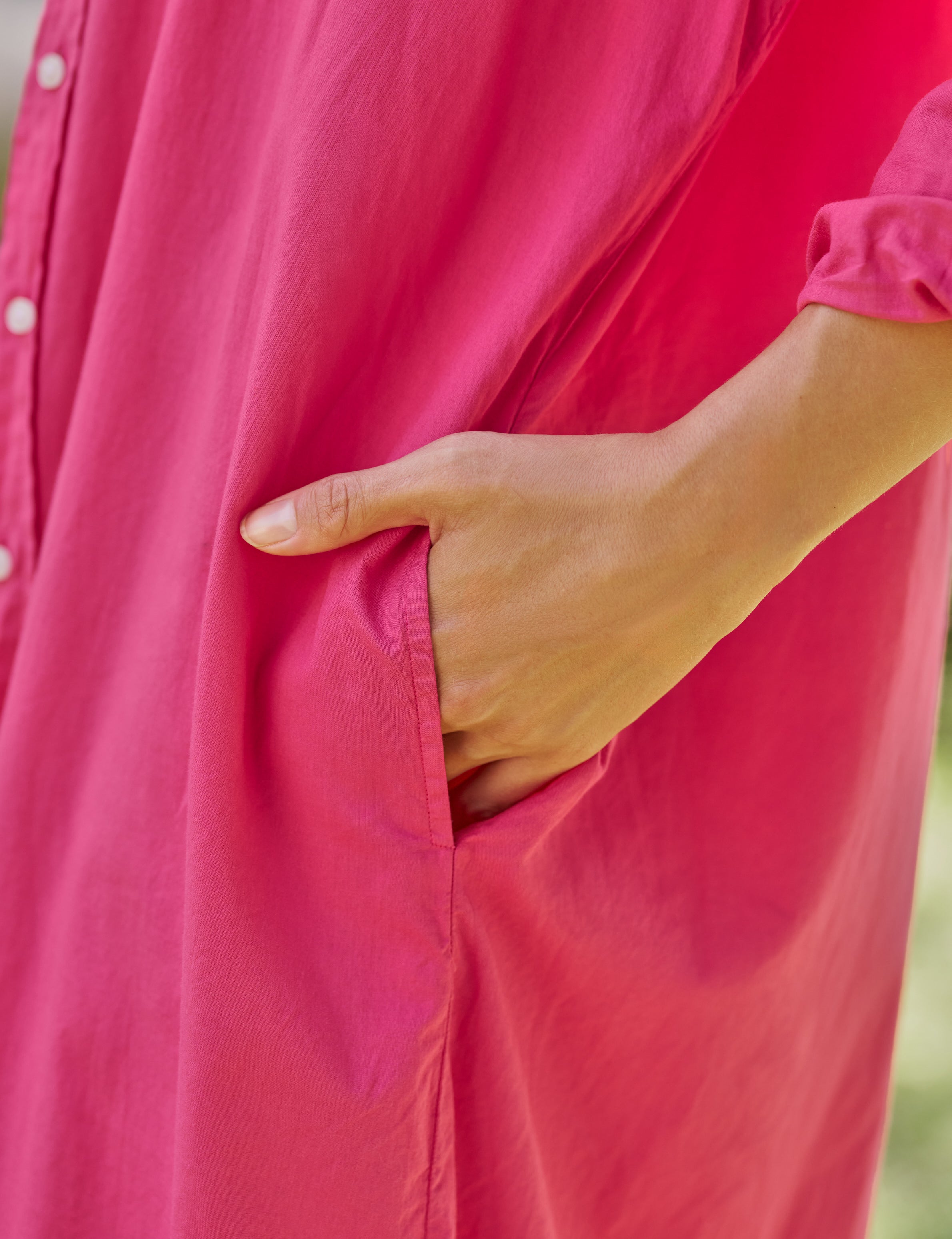 Person wearing a bright pink dress with a blurred background, view 3