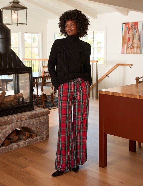 A woman stands in a bright, modern home interior wearing a black turtleneck sweater and red, green, and black plaid wide-leg pants., view 3