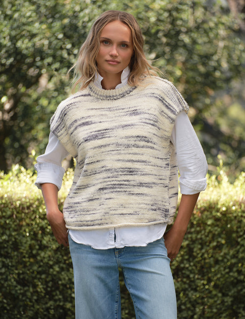Woman wearing a patterned vest over a white shirt with blue jeans outdoors., front view