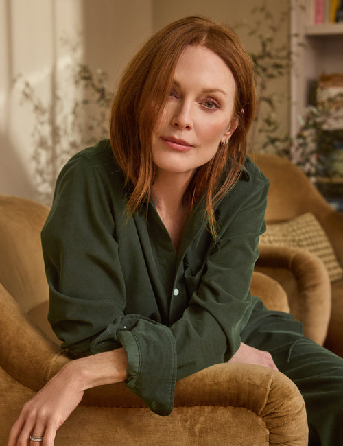 Woman sitting on a brown couch wearing a green shirt in a cozy room., alternate view