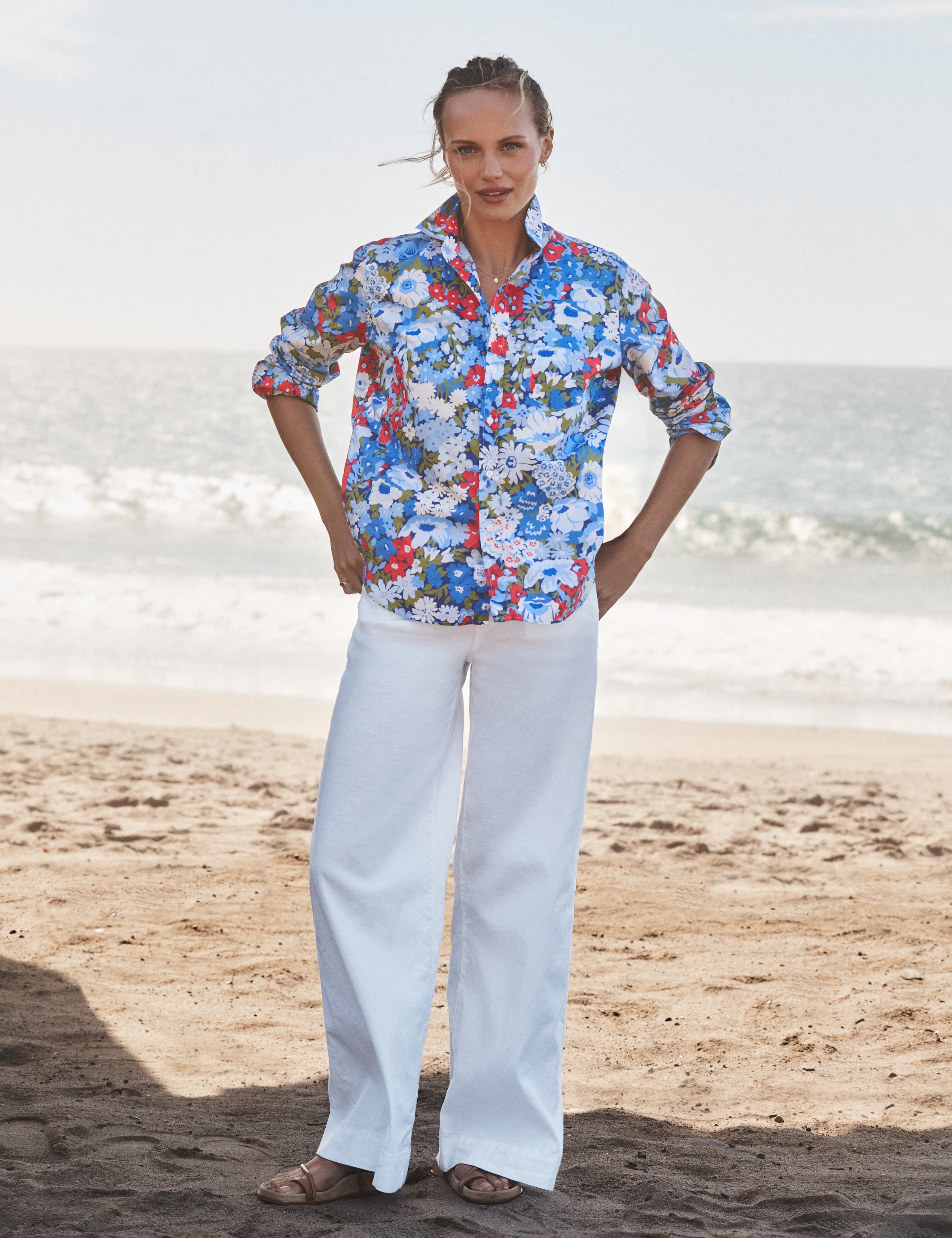 Woman wearing a colorful patterned shirt and white pants standing on a beach., view 4