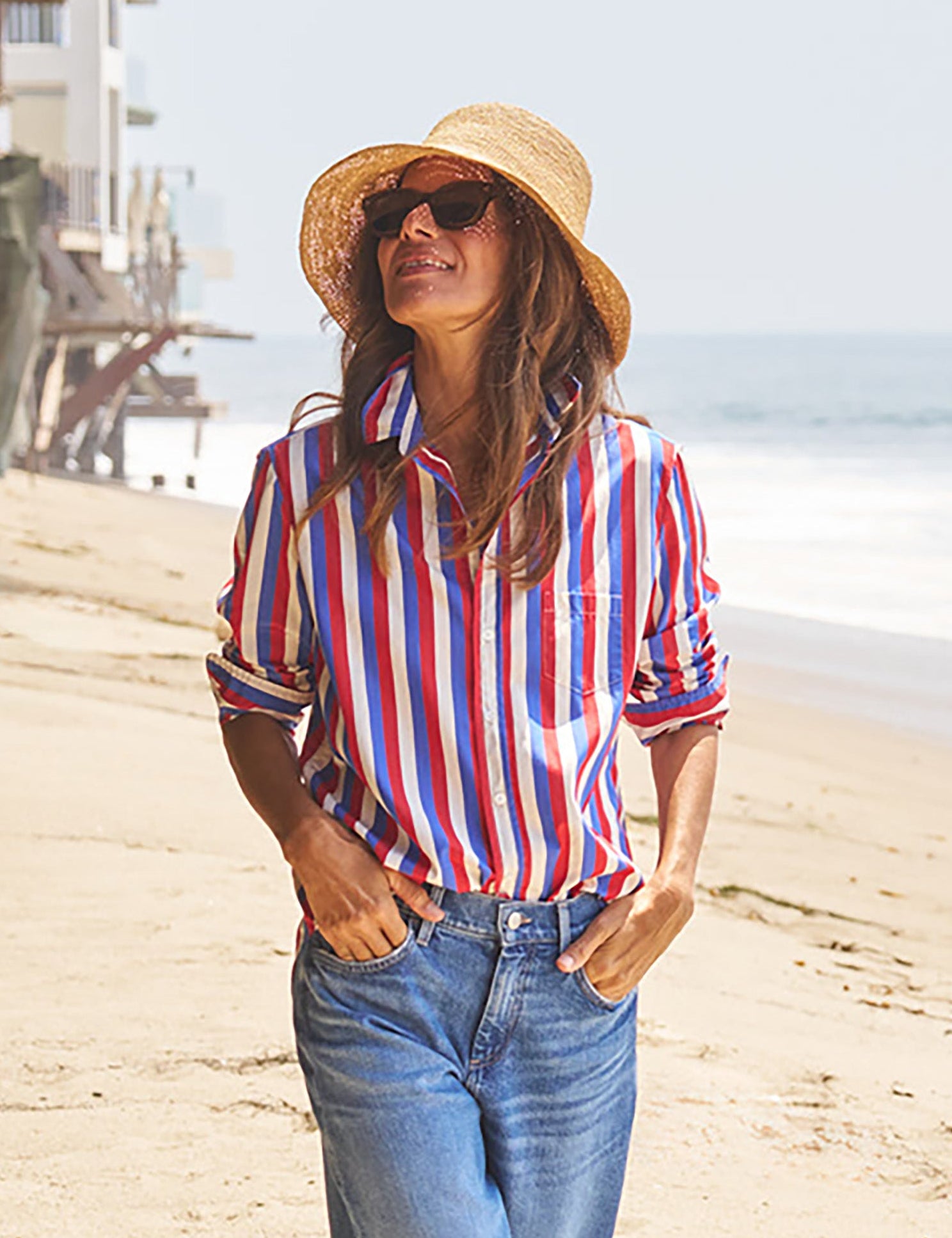 Woman wearing a colorful striped shirt and straw hat on a beach., front view