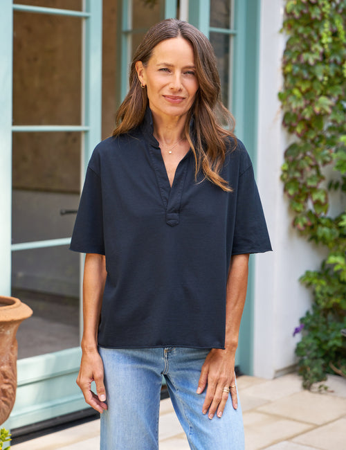 Woman wearing a navy shirt and blue jeans standing outdoors., front view