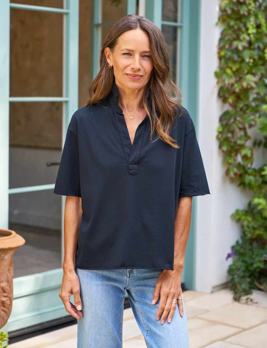 Woman wearing a navy shirt and blue jeans standing outdoors.