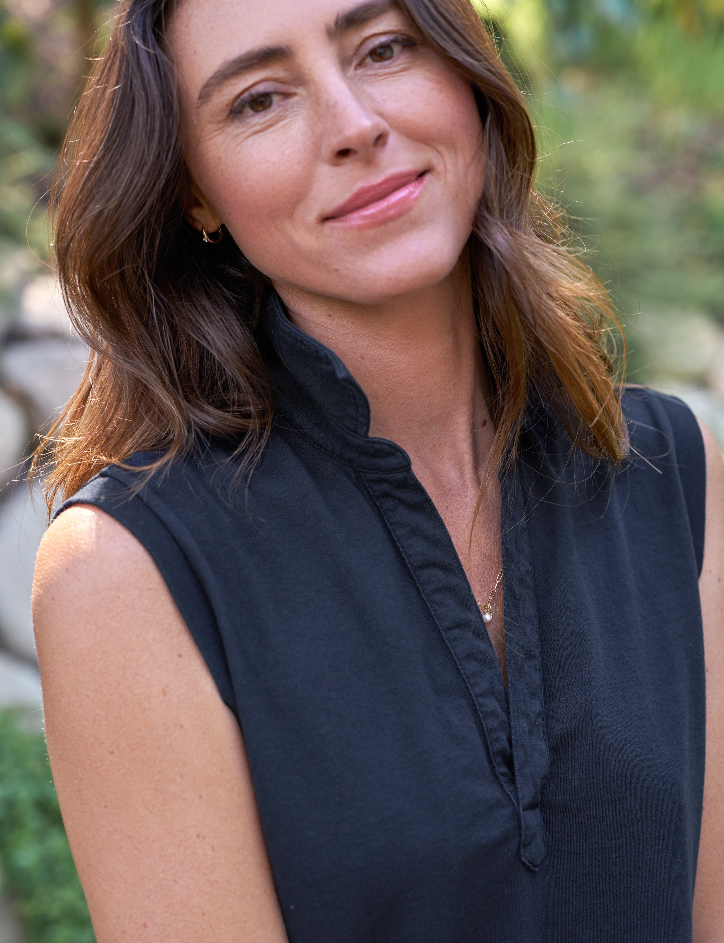 Woman wearing a navy sleeveless dress outdoors with greenery in the background, alternate view