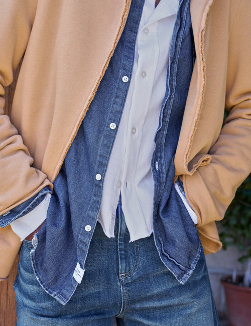 A close-up of a person wearing a tan blazer over a blue denim button-up shirt and white undershirt, paired with blue jeans., view 3