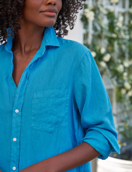 Person wearing a blue dress with a blurred outdoor background, view 3