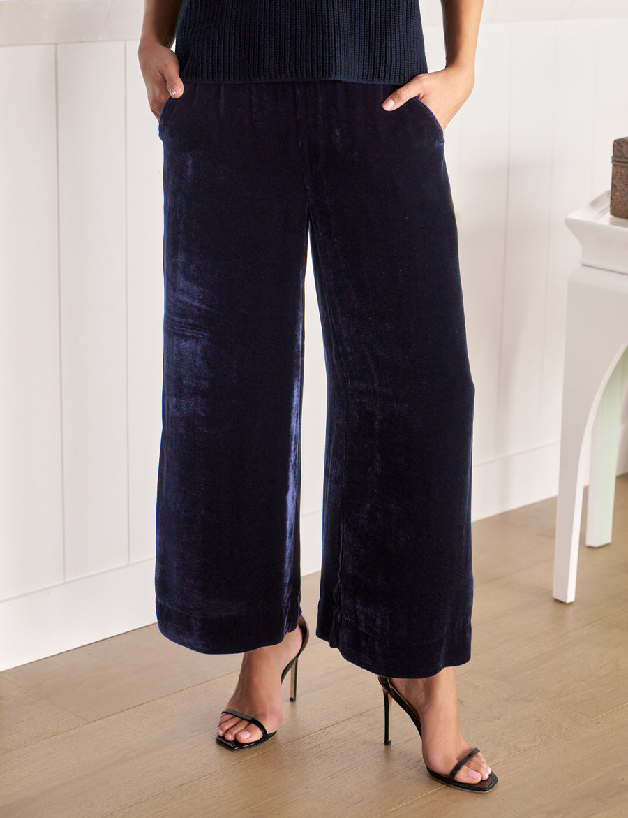 Person wearing navy velvet wide-leg pants and black high-heeled sandals in a minimal indoor setting.