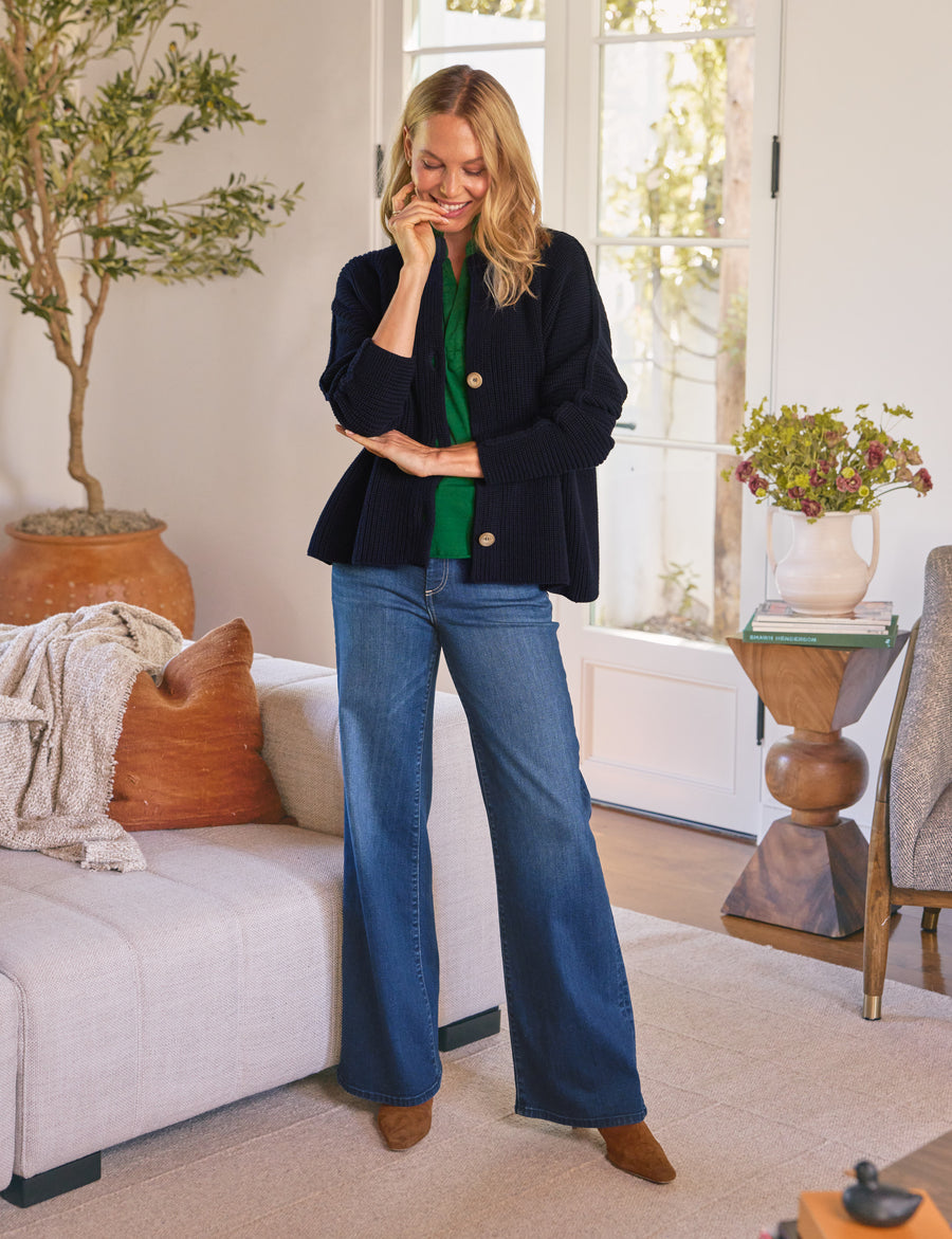 Woman in a living room wearing a navy blazer and blue jeans.