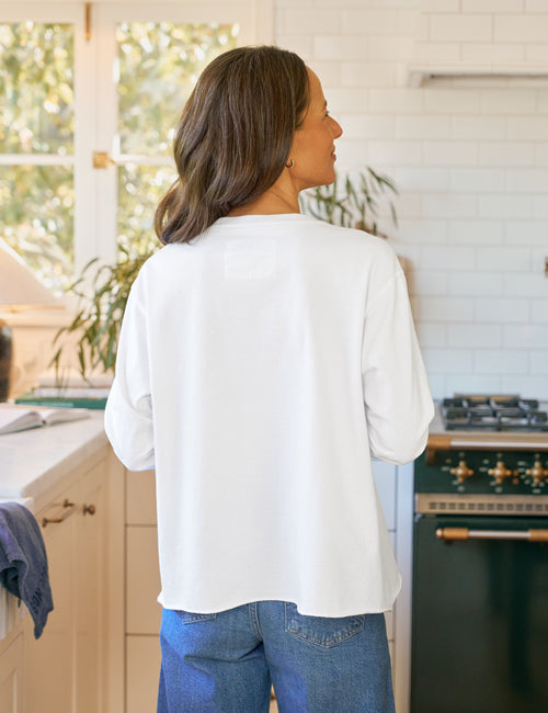 Woman standing in a kitchen wearing a white shirt and blue jeans., view 3
