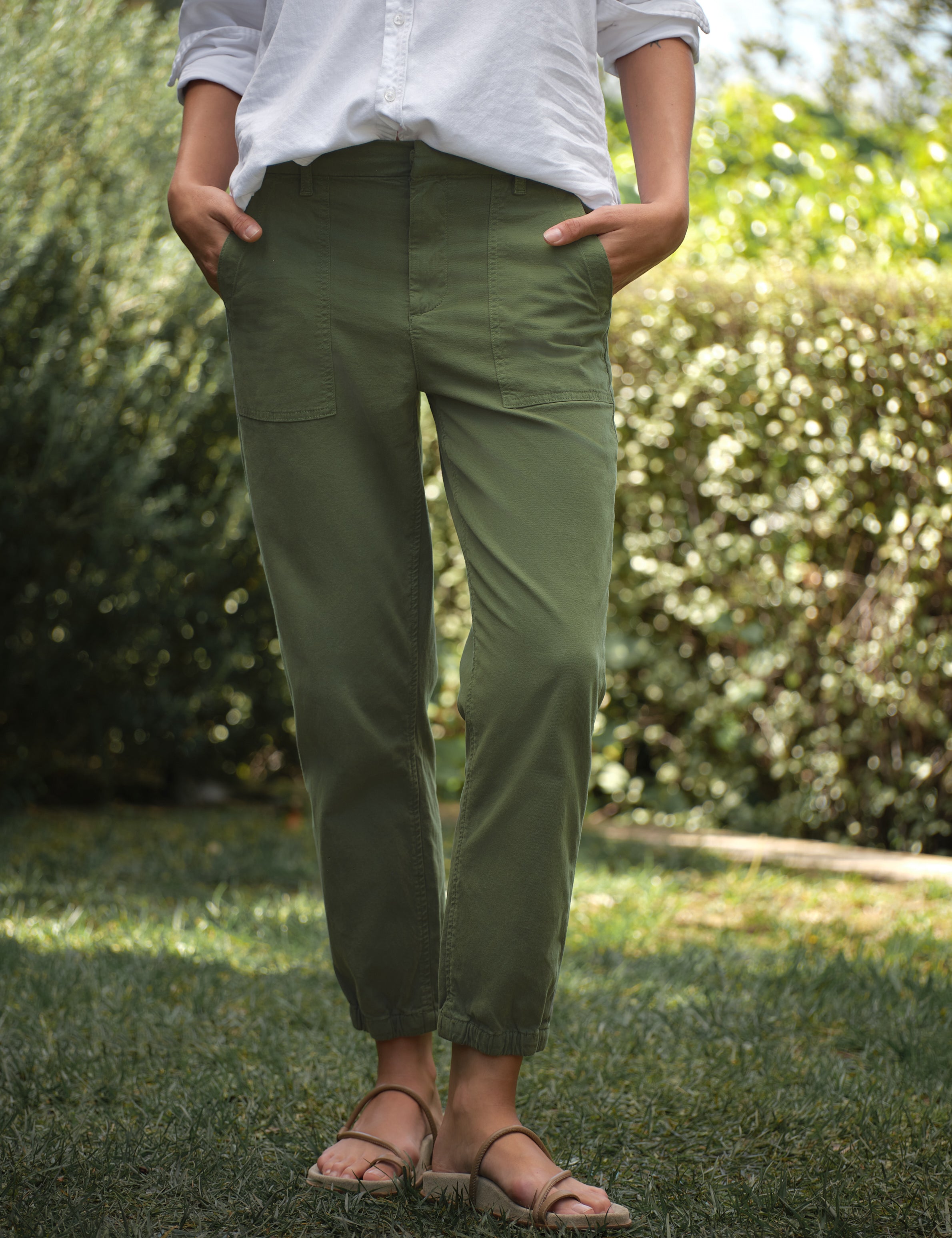 Person wearing green cargo pants standing in a grassy area with blurred greenery in the background, front view