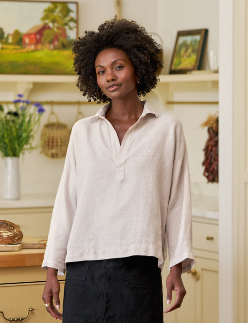 Woman standing in a kitchen wearing a light-colored blouse and black skirt., view 4