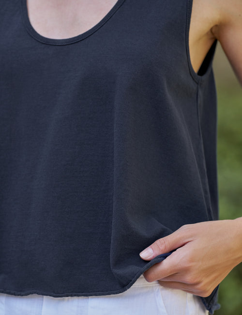 Person wearing a navy tank top with a blurred green background, view 3
