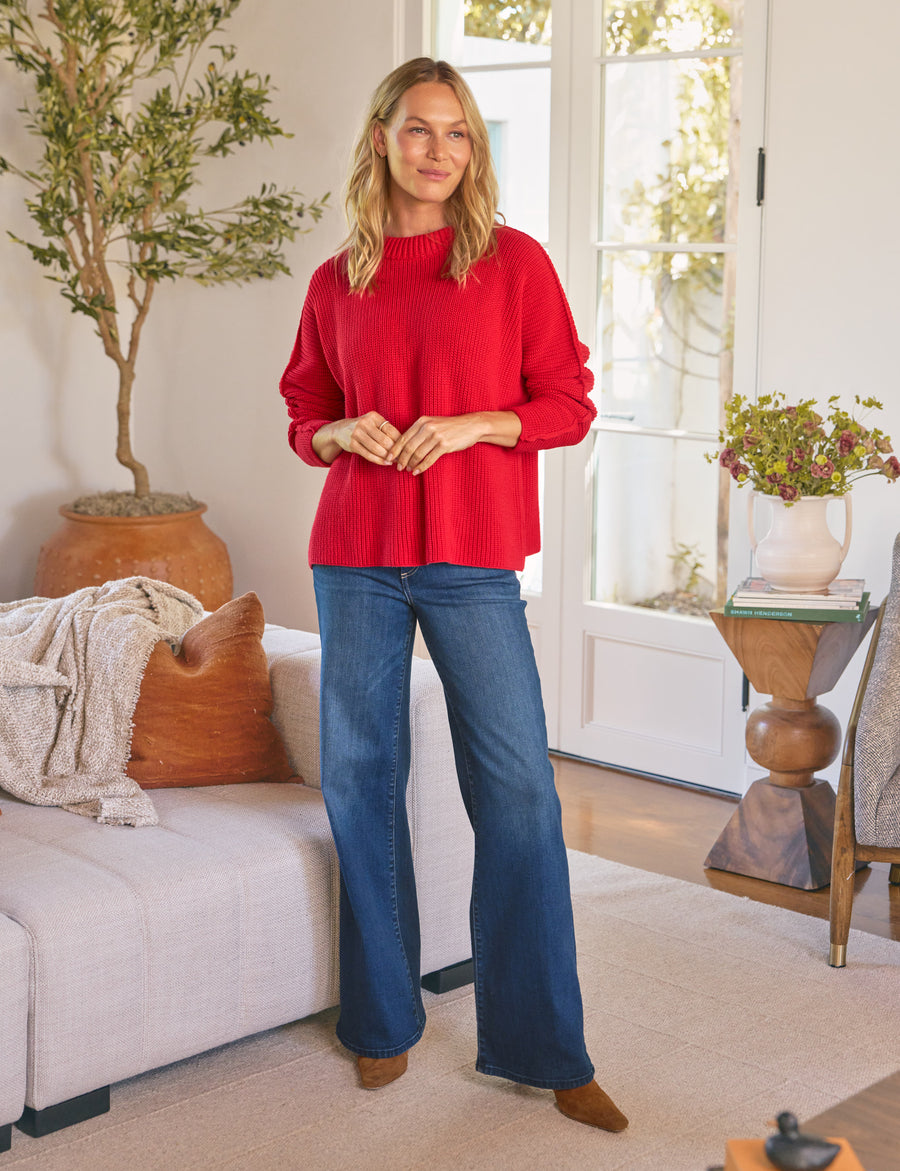 Woman wearing a red sweater and blue jeans standing in a living room.