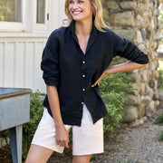 Woman wearing a black shirt and white shorts standing outdoors near a stone wall.