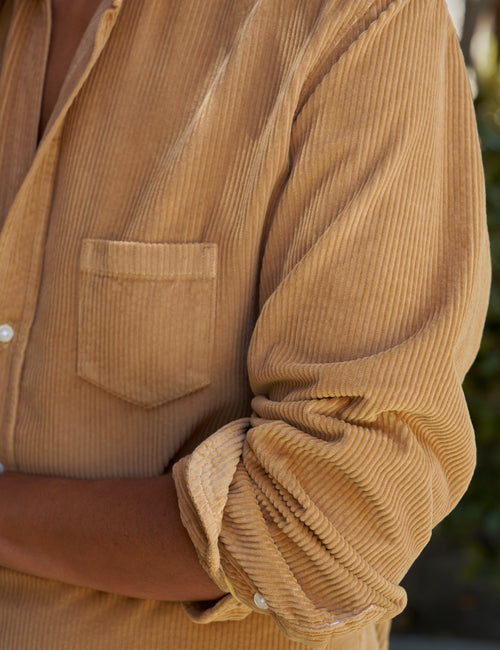 Close-up of a person wearing a tan corduroy button-up shirt with a chest pocket and rolled sleeves, photographed outdoors., view 3