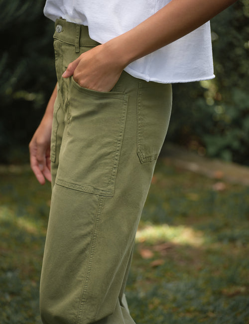 Person wearing green pants and a white shirt with a blurred natural background, view 3