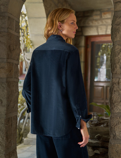 A woman wearing a dark navy blue long-sleeve shirt and matching pants, standing in a stone archway doorway., alternate view