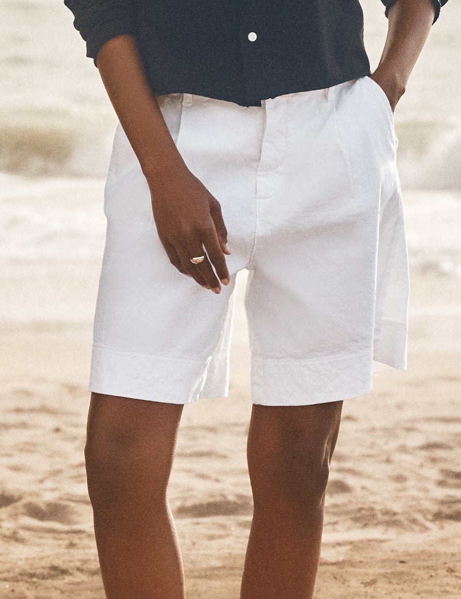 Woman standing on a beach wearing a navy shirt and white shorts., front view
