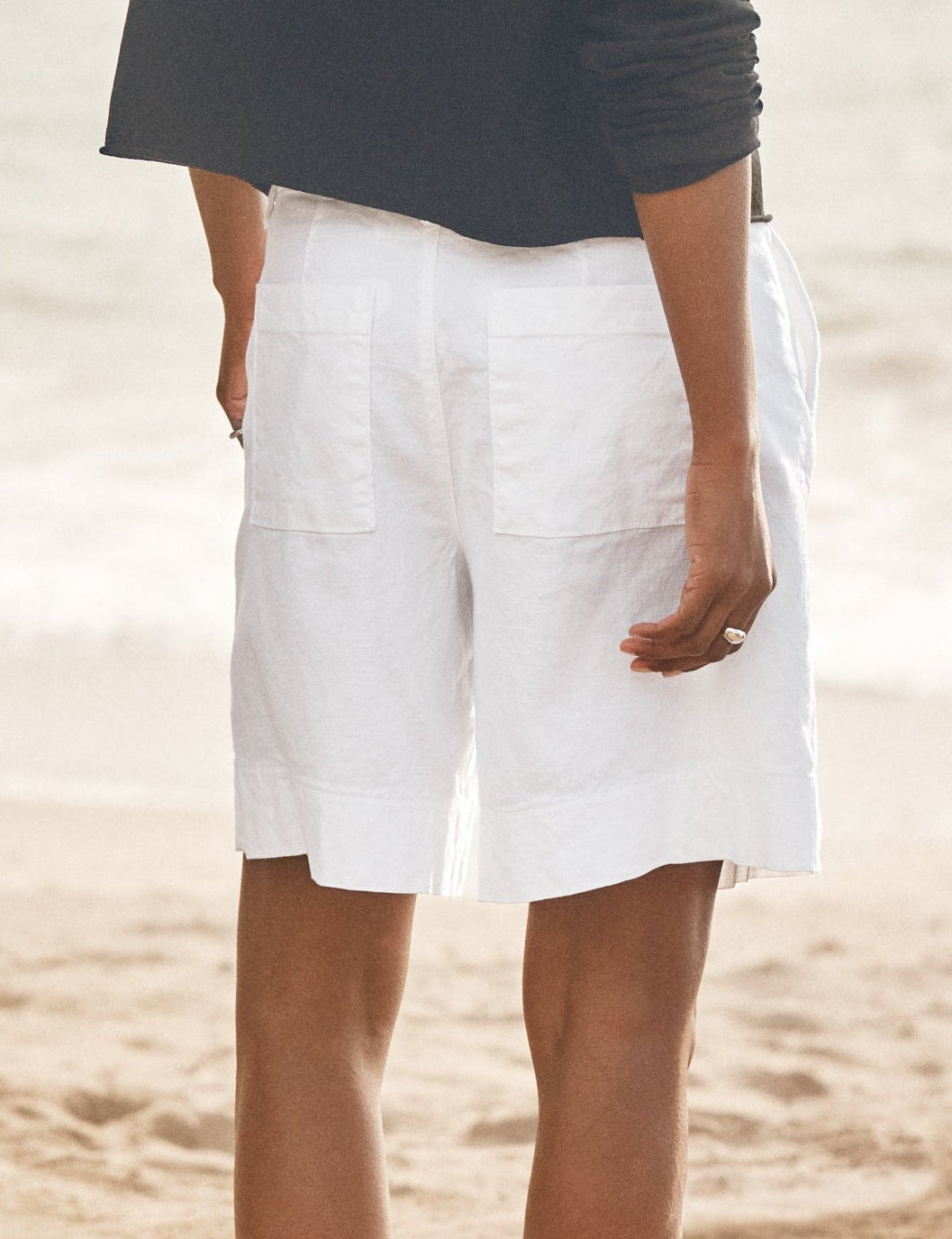 Person wearing a dark shirt and white shorts standing on a beach., alternate view