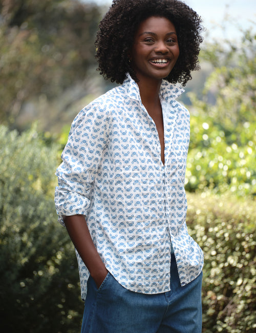 Woman wearing a white patterned shirt with rolled-up sleeves and blue jeans standing outdoors., front view