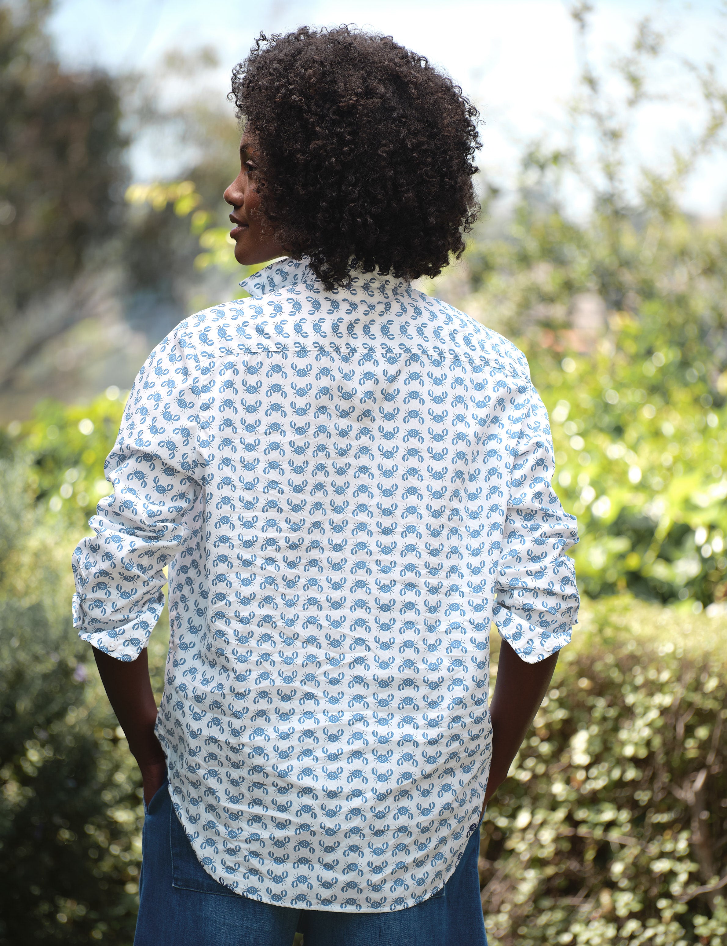 Person wearing a patterned shirt standing outdoors with greenery in the background, alternate view
