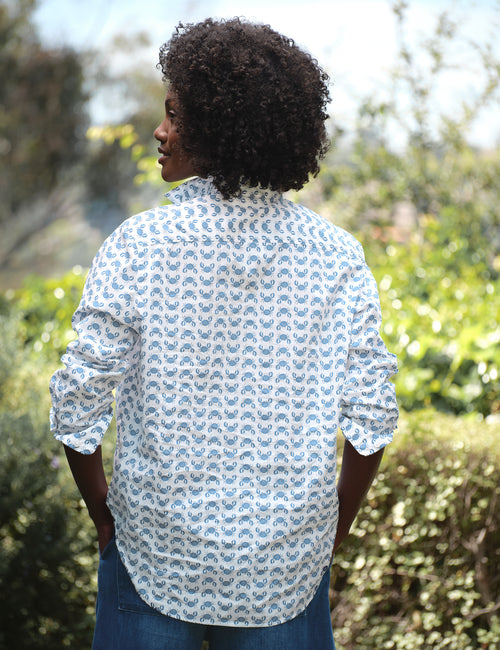 Person wearing a patterned shirt standing outdoors with greenery in the background, alternate view