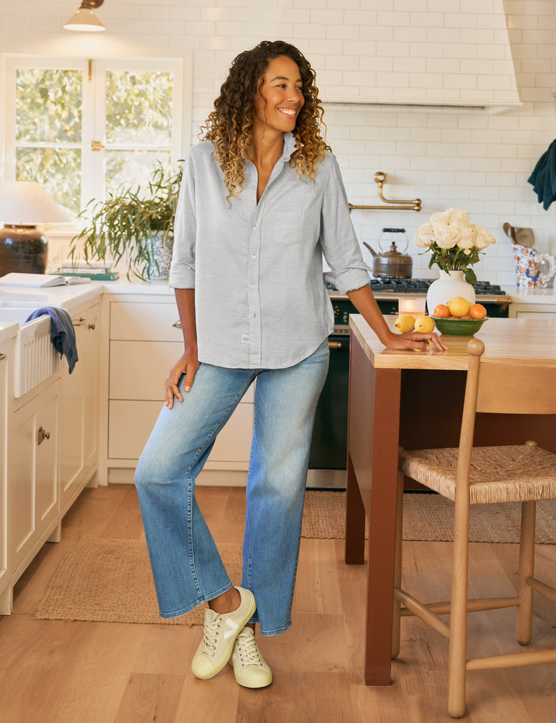 Woman standing in a kitchen wearing a light gray shirt and jeans.