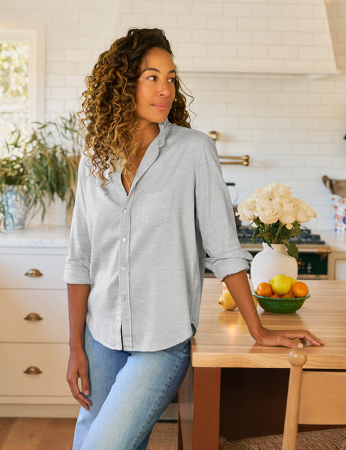 Woman standing in a kitchen wearing a light gray button-up shirt and blue jeans., front view