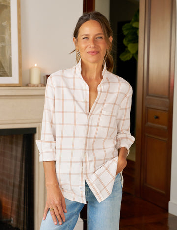 Woman wearing a white plaid shirt and blue jeans standing in a room with a fireplace.